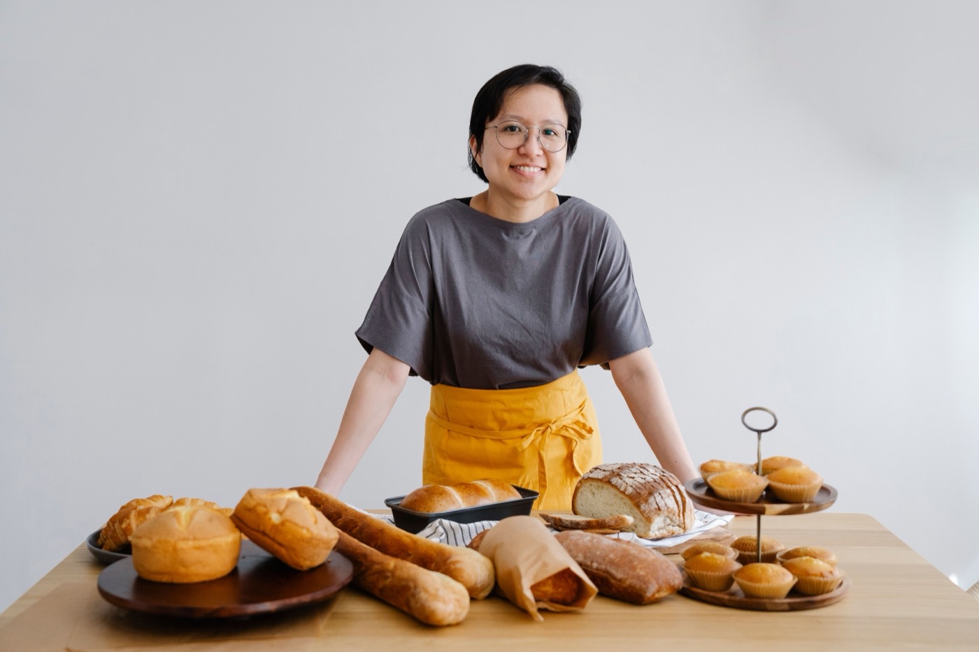 A smiling baker standing behind a table of freshly baked bread