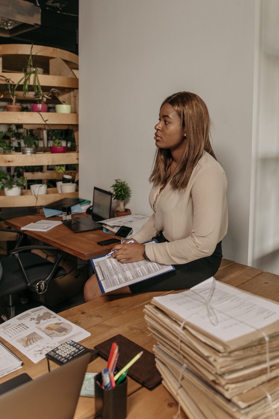 A business owner working at her desk beside tall stacks of bundled paperwork
