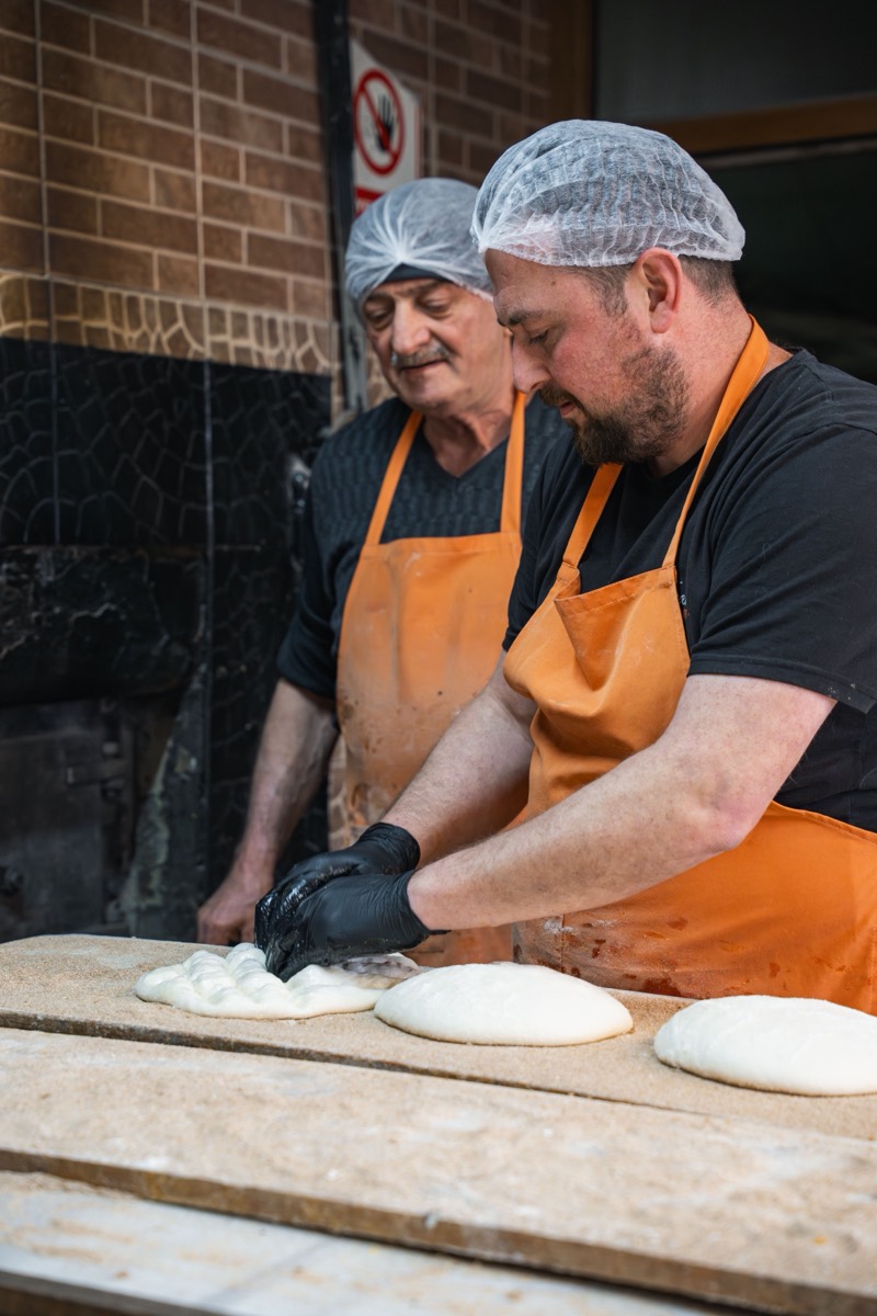 Two pizzaiolos shaping fresh dough on a wooden counter
